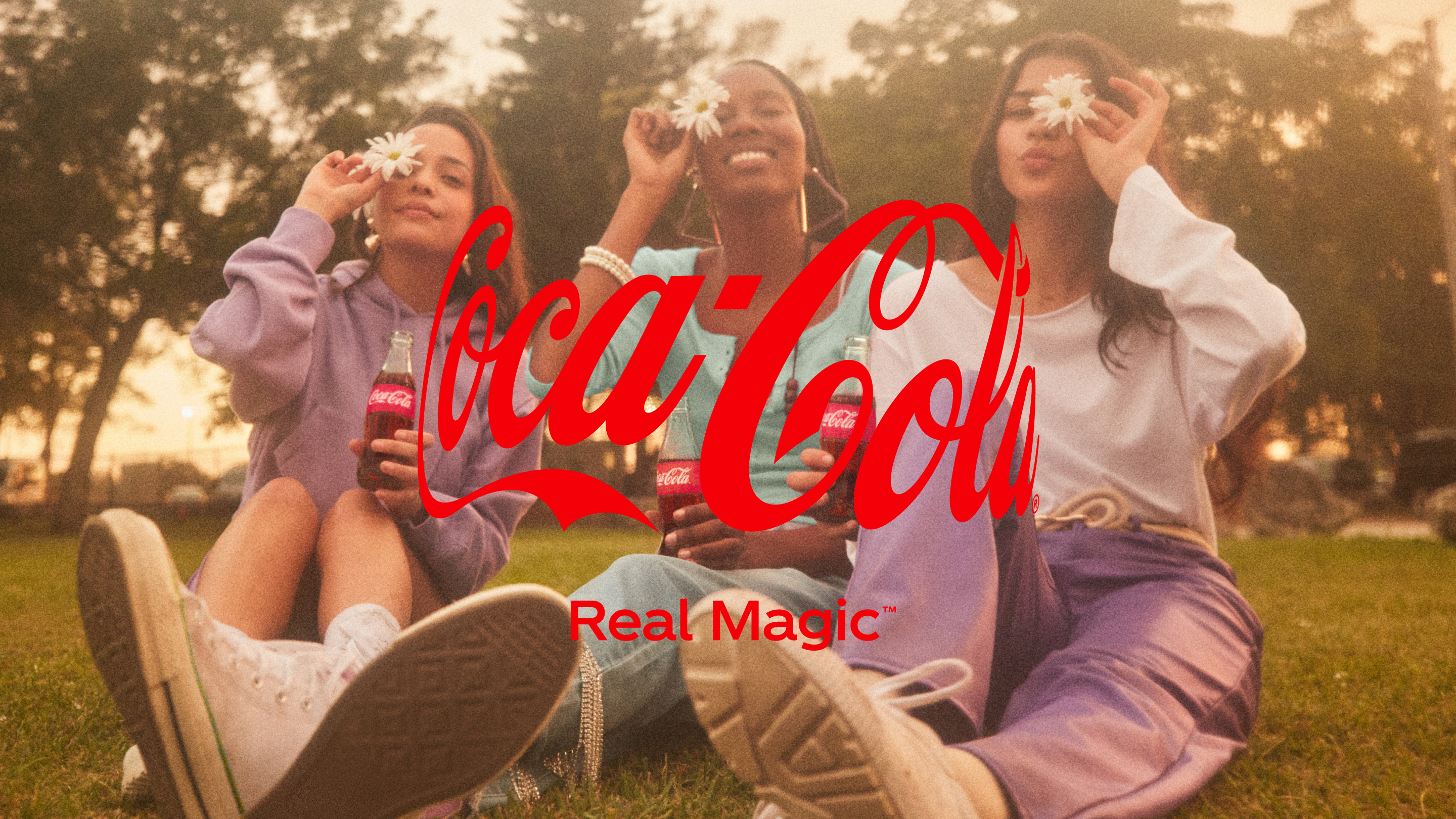 Mladé ženy sedící na trávě si užívají své okolí s přikrývkou s logem Coca-Cola
